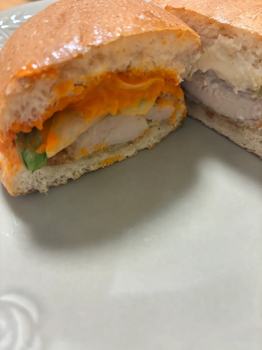 レッドホットソースのバーガーの断面。チキンとオレンジ色のソースが見える